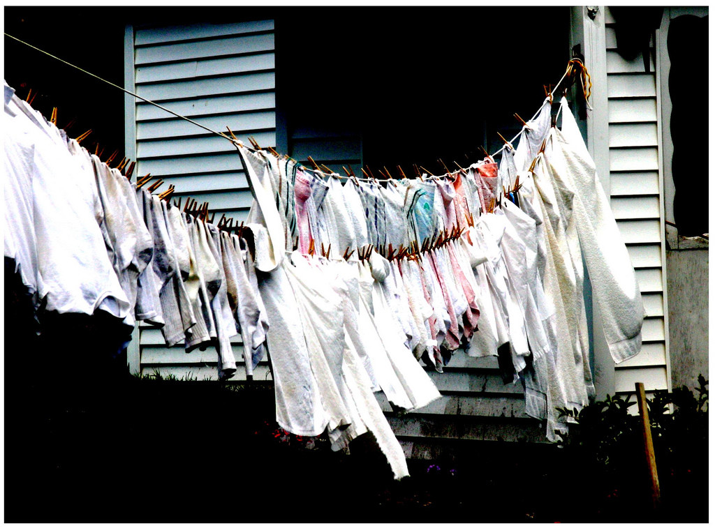 Rows of white laundry clothing hanging on a clothesline against a house wall, muted tones, everyday domestic mood.
